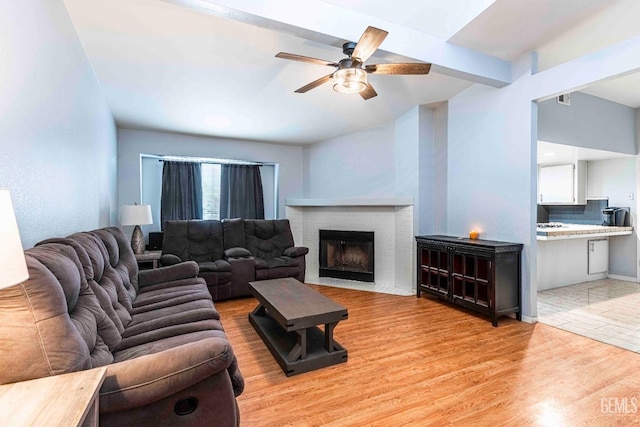 living room featuring a wealth of natural light, beam ceiling, light wood-style floors, a fireplace, and ceiling fan