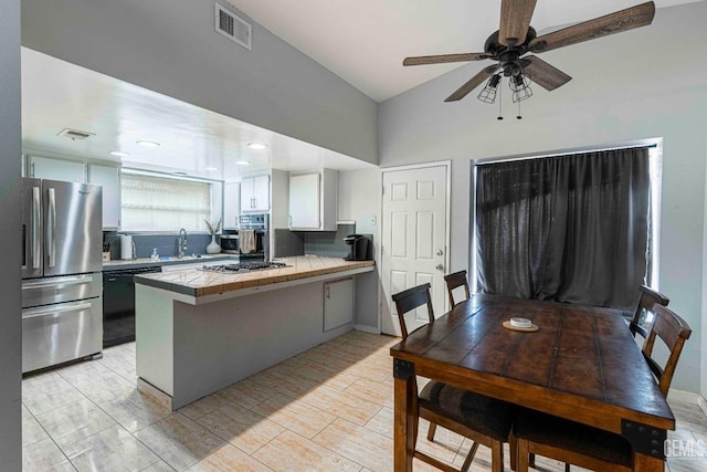 kitchen featuring visible vents, a sink, stainless steel appliances, a peninsula, and tile counters