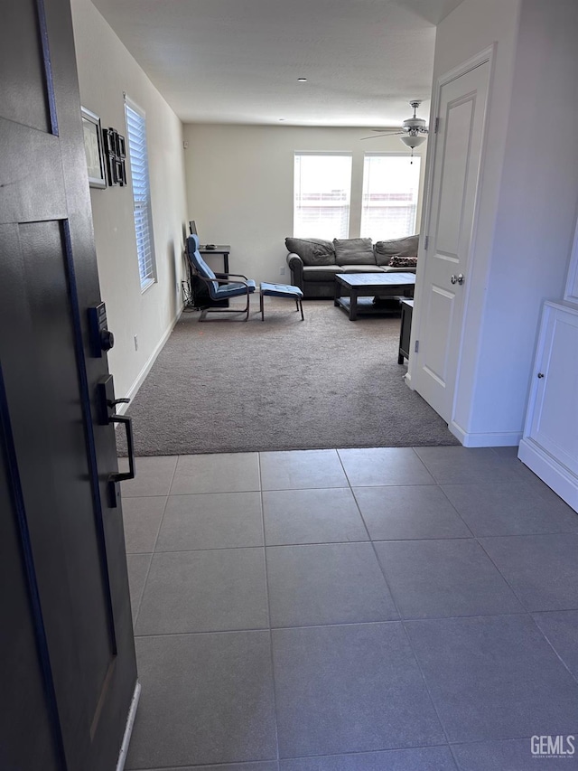 tiled living area with carpet floors, a ceiling fan, and baseboards