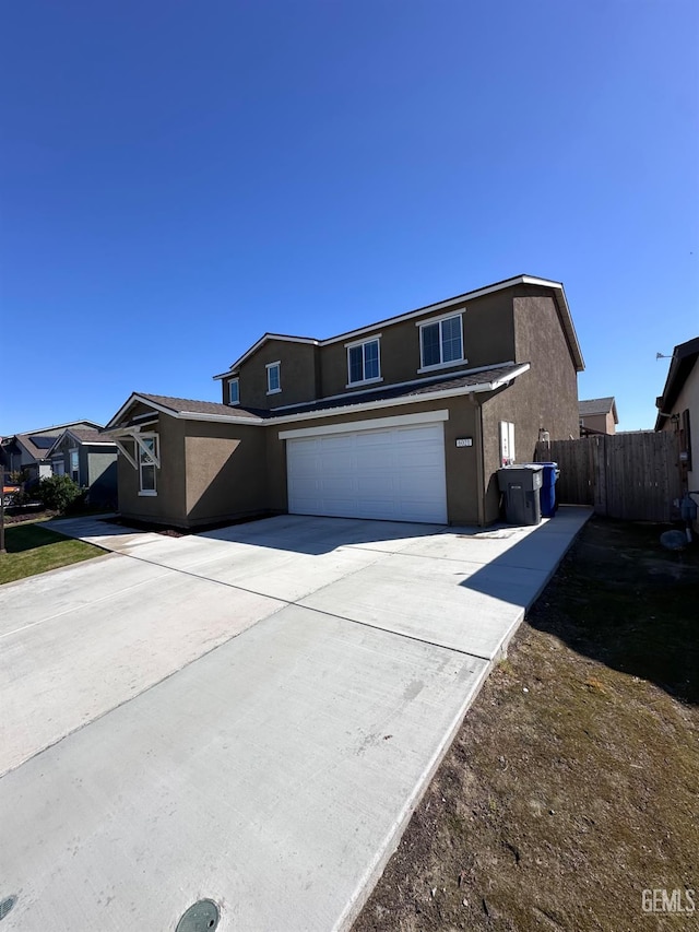 traditional-style house with concrete driveway, an attached garage, fence, and stucco siding