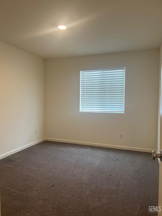 unfurnished room featuring dark carpet and baseboards