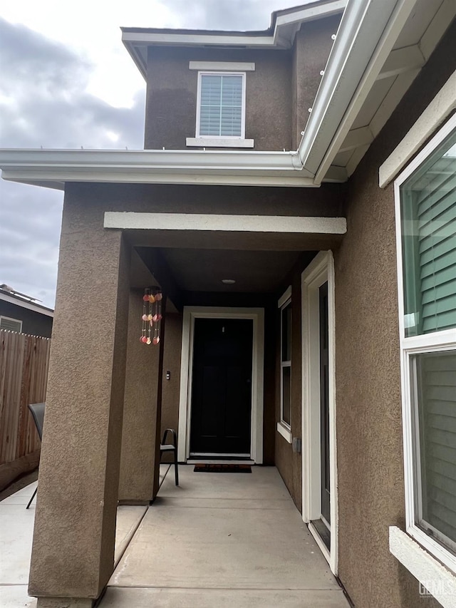 view of exterior entry featuring fence and stucco siding