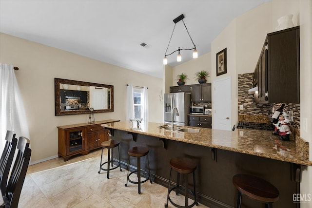 kitchen featuring stone countertops, a breakfast bar, kitchen peninsula, dark brown cabinetry, and stainless steel fridge with ice dispenser