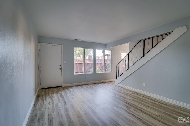 unfurnished living room with stairway, visible vents, baseboards, and wood finished floors