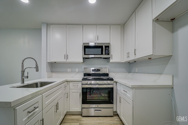 kitchen featuring light stone counters, a peninsula, a sink, white cabinetry, and appliances with stainless steel finishes