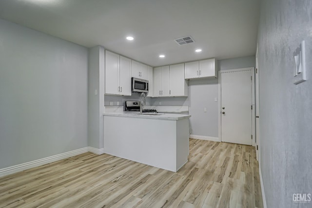 kitchen with visible vents, appliances with stainless steel finishes, white cabinets, a sink, and a peninsula