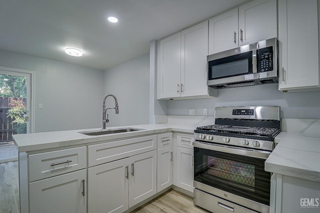 kitchen featuring a peninsula, a sink, white cabinets, appliances with stainless steel finishes, and light stone countertops