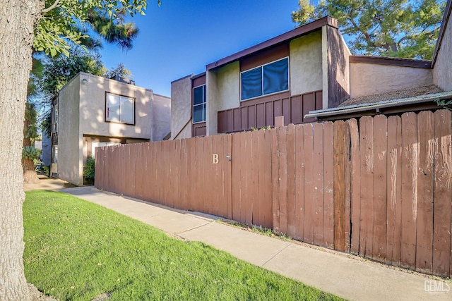 view of side of property with fence, a lawn, and stucco siding