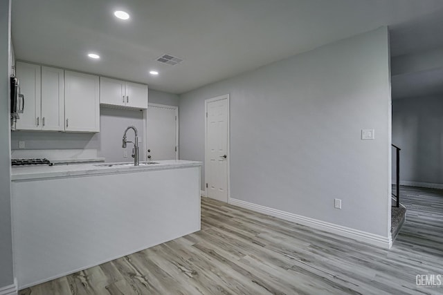 kitchen featuring visible vents, stainless steel microwave, light wood-type flooring, white cabinetry, and a sink