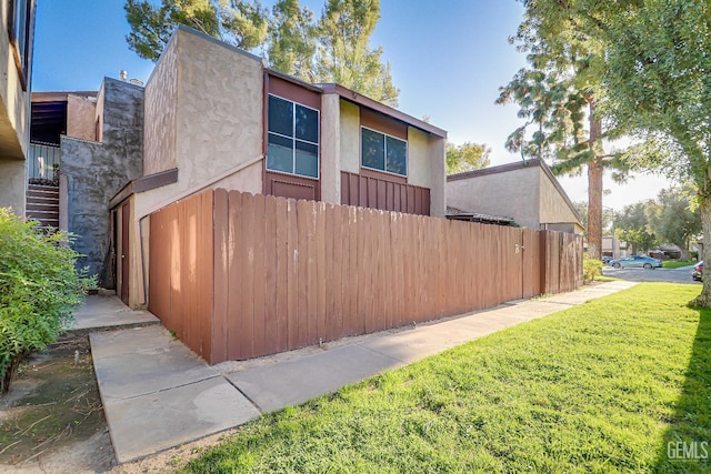 view of side of home with a yard, stairway, fence, and stucco siding