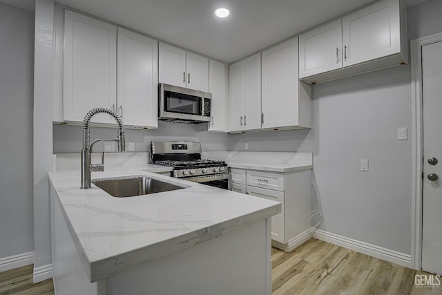 kitchen featuring white cabinets, a peninsula, light stone countertops, stainless steel appliances, and a sink