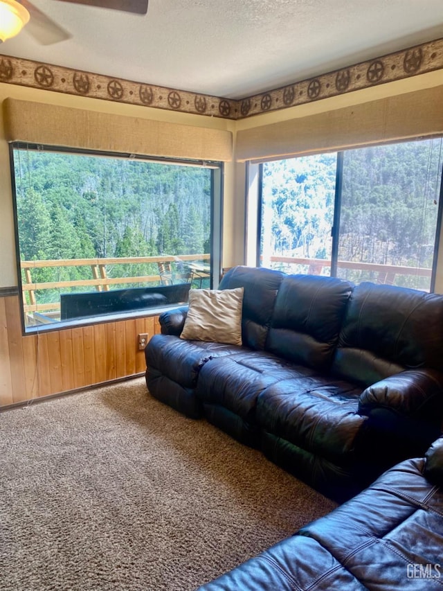 carpeted living room featuring ceiling fan, a textured ceiling, and wooden walls