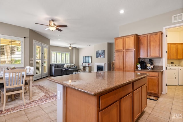 5703 Park Pl, Bakersfield, CA 93306 - kitchen featuring washing machine and dryer, ceiling fan, a center island, light tile patterned flooring, and dark stone countertops