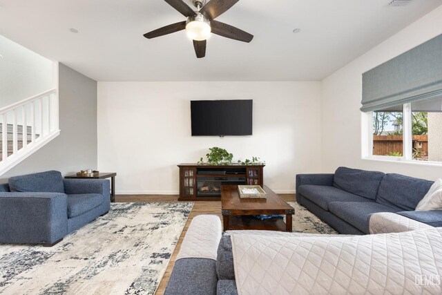 living room featuring a ceiling fan, stairs, baseboards, and wood finished floors