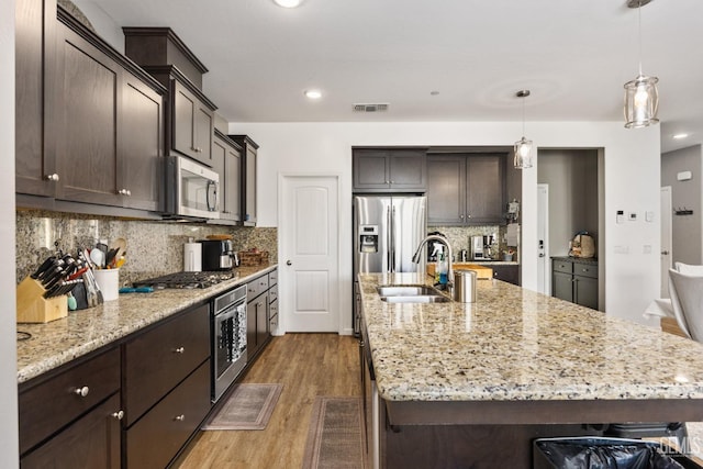 kitchen with a spacious island, dark brown cabinets, wood finished floors, stainless steel appliances, and a sink