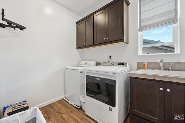 washroom with baseboards, light wood-style flooring, washer and dryer, cabinet space, and a sink