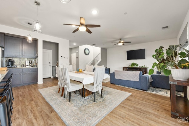 dining room featuring visible vents, light wood-style flooring, stairway, and ceiling fan