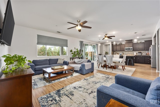 living room with visible vents, light wood-style floors, and a ceiling fan