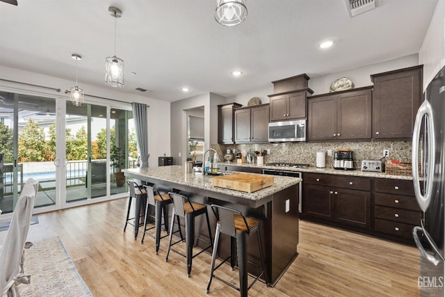 kitchen with visible vents, a sink, stainless steel appliances, decorative backsplash, and dark brown cabinets