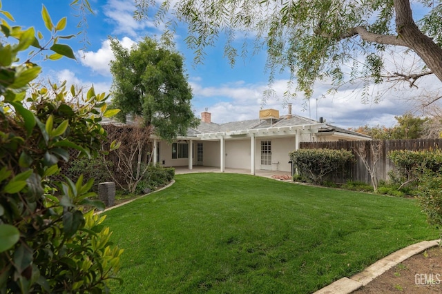 rear view of house with fence, a yard, stucco siding, a chimney, and a patio area