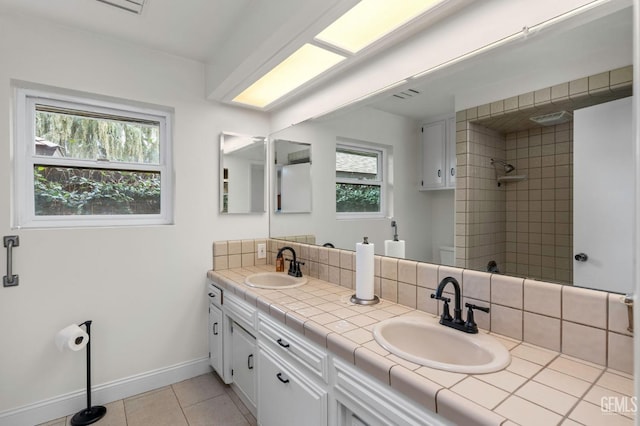 full bathroom featuring a sink, a tile shower, baseboards, and double vanity