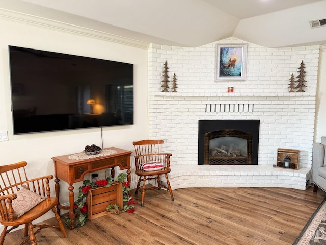 sitting room with a fireplace, wood-type flooring, lofted ceiling, and ornamental molding