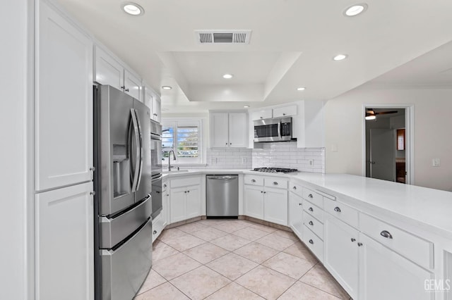 kitchen featuring visible vents, white cabinets, decorative backsplash, appliances with stainless steel finishes, and a tray ceiling