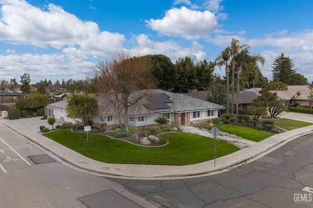 ranch-style house featuring solar panels, an attached garage, a residential view, driveway, and a front lawn