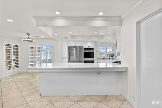 kitchen with stainless steel appliances, white cabinets, ornamental molding, and a peninsula