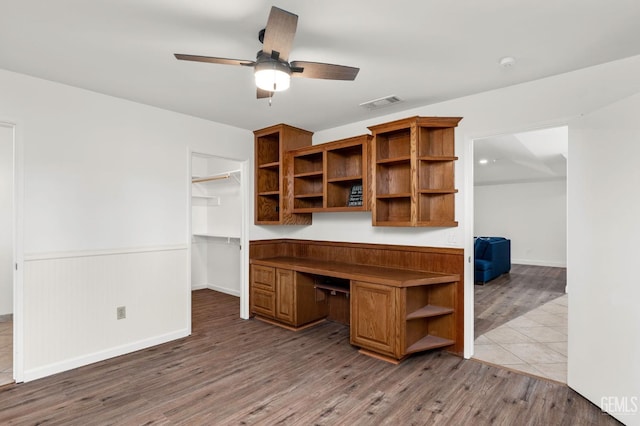 unfurnished office with visible vents, a ceiling fan, wainscoting, built in study area, and wood finished floors