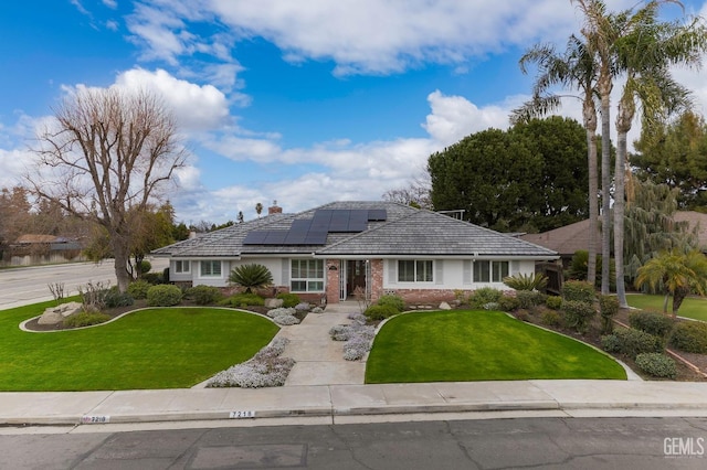 ranch-style house with brick siding, roof mounted solar panels, a chimney, and a front yard