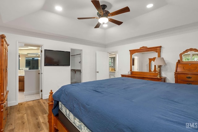 bedroom featuring ensuite bathroom, a tray ceiling, wood-type flooring, a walk in closet, and crown molding