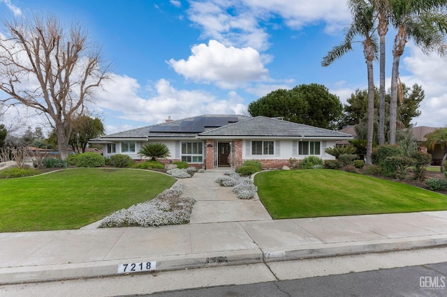 ranch-style home featuring solar panels, a front lawn, and brick siding