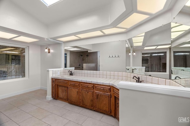 kitchen featuring brown cabinets, light tile patterned floors, a sink, a peninsula, and baseboards