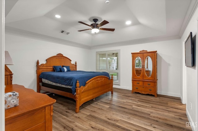 bedroom featuring wood finished floors, visible vents, baseboards, ornamental molding, and a tray ceiling