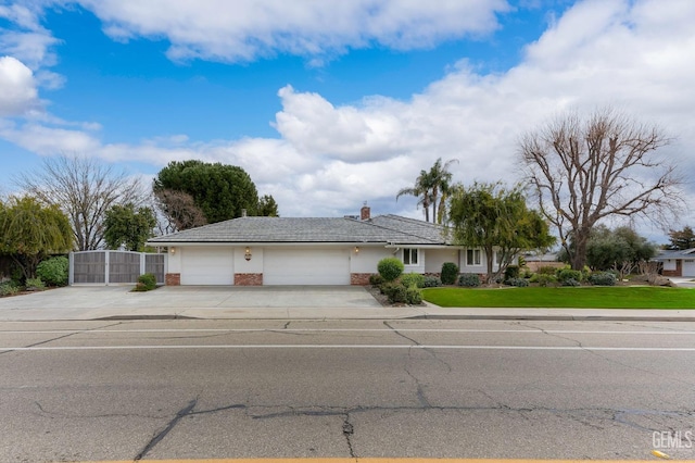 ranch-style house featuring a chimney, concrete driveway, a gate, a garage, and a front lawn