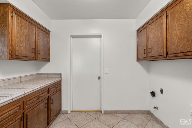 laundry room featuring light tile patterned floors, hookup for a gas dryer, cabinet space, hookup for an electric dryer, and baseboards