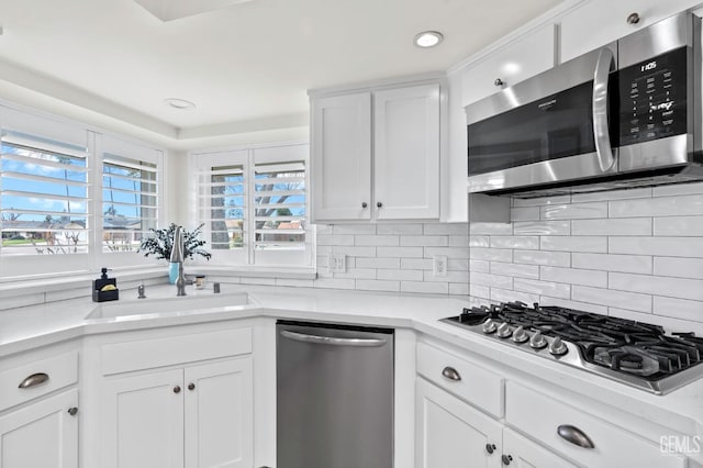 kitchen featuring stainless steel appliances, light countertops, decorative backsplash, white cabinetry, and a sink