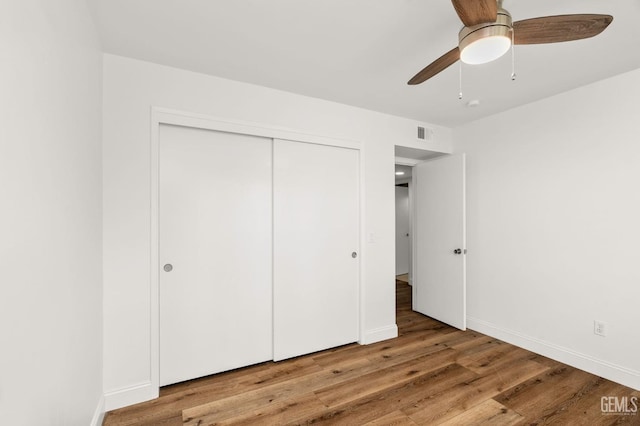 unfurnished bedroom featuring ceiling fan, wood finished floors, visible vents, baseboards, and a closet