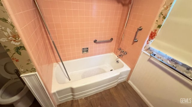 bathroom with tiled shower / bath combo, wood-type flooring, and toilet