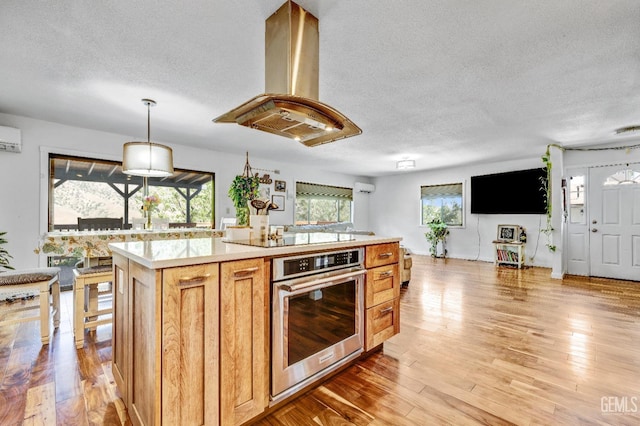 kitchen featuring stainless steel oven, black electric stovetop, decorative light fixtures, a kitchen island, and island exhaust hood