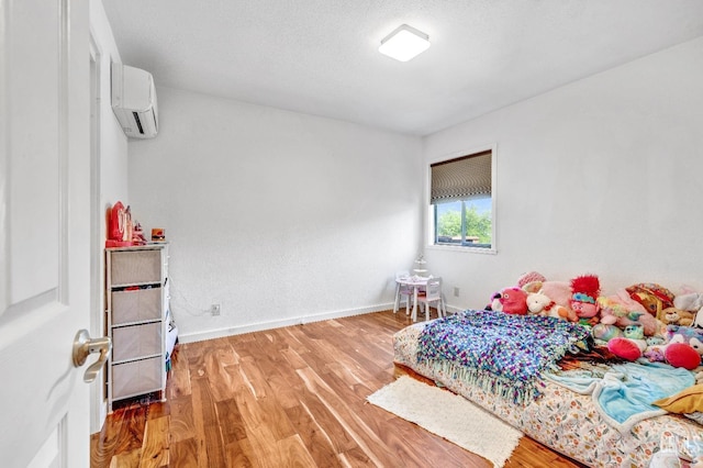 bedroom with hardwood / wood-style floors, a textured ceiling, and a wall unit AC