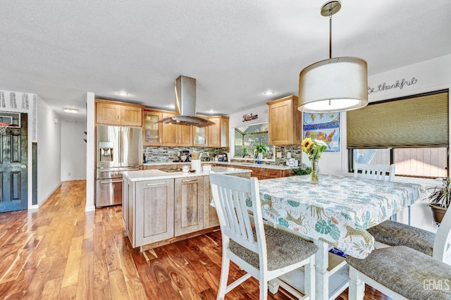 kitchen featuring stainless steel fridge, backsplash, island range hood, light hardwood / wood-style flooring, and a center island