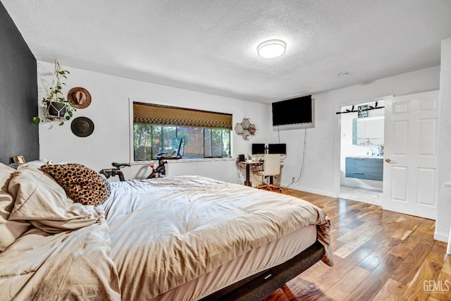 bedroom with ensuite bathroom, wood-type flooring, and a textured ceiling