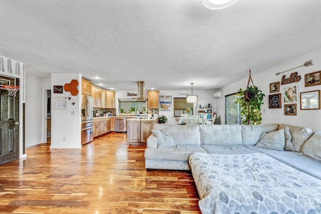 living room featuring a wall mounted air conditioner, light wood-type flooring, and a textured ceiling