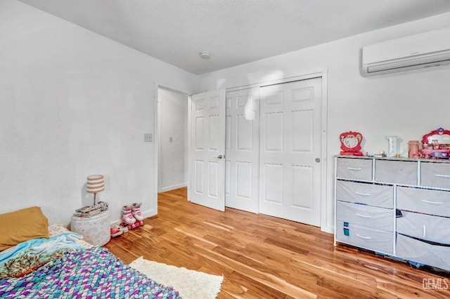 bedroom with a closet, a wall mounted air conditioner, and light hardwood / wood-style flooring