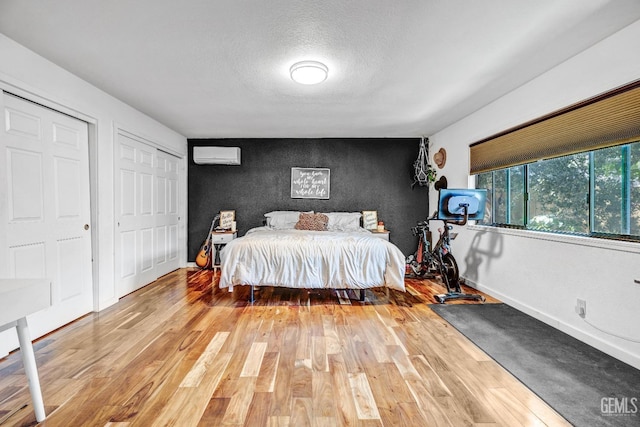 bedroom featuring a wall mounted air conditioner, a textured ceiling, hardwood / wood-style flooring, and multiple closets