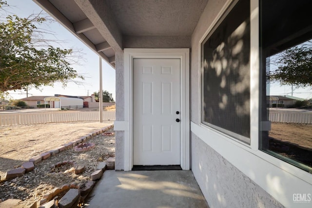 entrance to property featuring stucco siding and fence