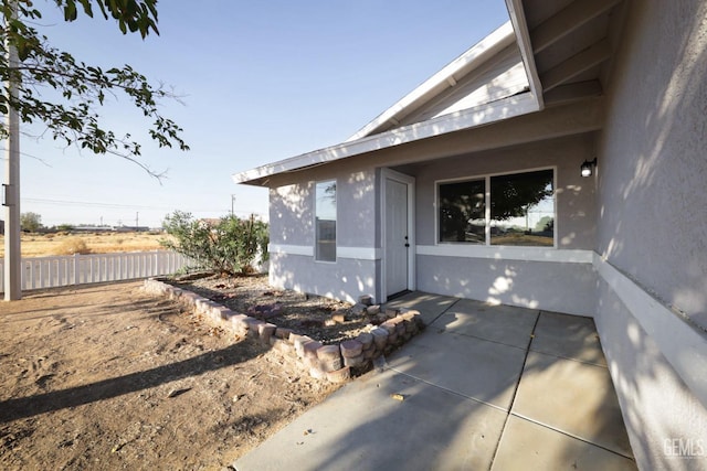 view of property exterior featuring a patio, stucco siding, and fence
