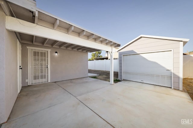 view of patio with concrete driveway, an outbuilding, a garage, and fence